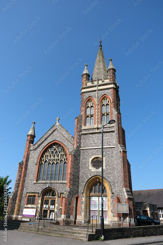 Fototapeta premium Methodist Church Building with Tall Steeple and Stained Glass Window Under Clear Blue Sky, Petersfield