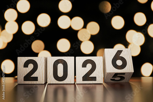 Wooden New Year 2026 cubes stand on a wooden table against a golden bokeh background. 2026 replaces 2025, a creative idea. New Year's Eve. 6 changes 5