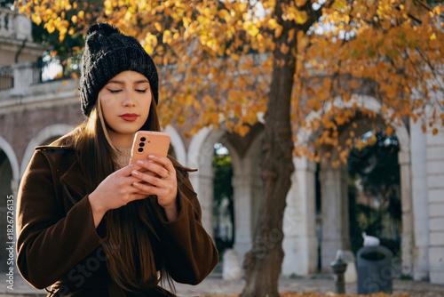 Mujer joven enviando mensajes de texto mientras disfruta de un descanso en el parque.
