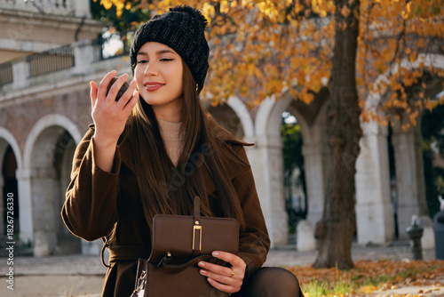 Mujer joven con abrigo marrón y gorro de invierno  en un entorno de parque con árboles de otoño