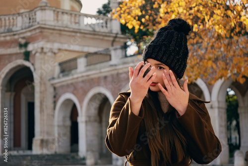 Mujer joven con abrigo marrón y gorro de invierno  en un entorno de parque con árboles de otoño