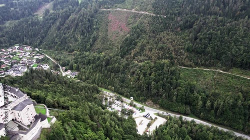 Reverse drone flight over Werfen Castle parking lot with mountain backdrop
