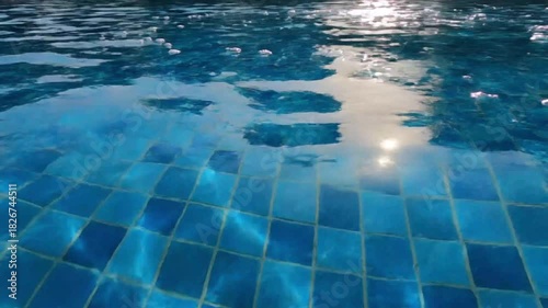 Swimming pool water surface with sunlight reflection and blue tile floor