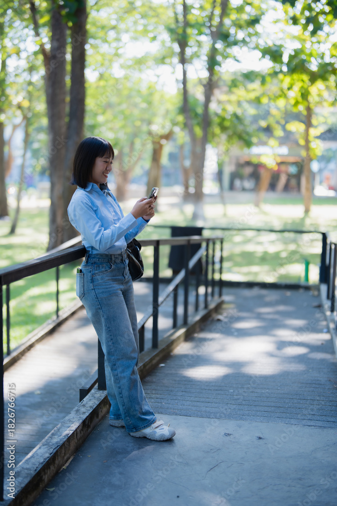 Fototapeta premium Young asian woman smiling using smartphone in park