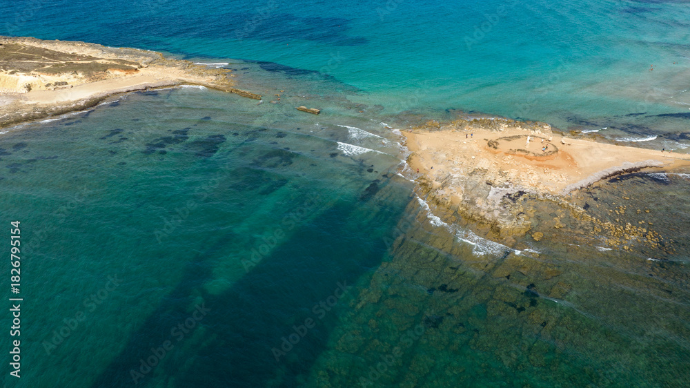 Obraz premium Aerial view of the isthmus separating Isola delle Correnti from Sicily, Italy. The sea is clean and crystal clear. It is the southernmost point of Italy. It is a sunny summer day.