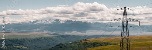 A highvoltage power line stands tall against a backdrop of rolling hills and majestic mountains in the distance