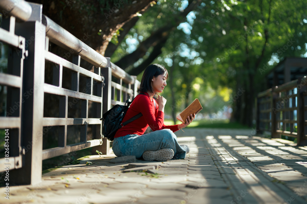 Fototapeta premium Young woman reading book outdoors in park