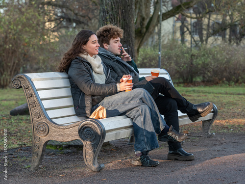 Man and woman sitting on a park bench and drinking coffee