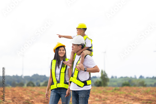 piggy back Asian Engineer family in field with wind turbines in background, Windmill. environmental renewable clean energy. Wind power generation. Solar panel. Windmill engineer inspection progress