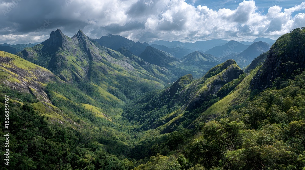 Naklejka premium Towering emerald peaks rise above a densely forested valley under a dramatic cloudy sky