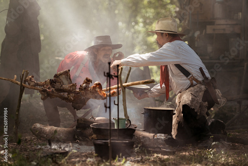 Two cowboys preparing food at a campfire, roasting meat together in a warm