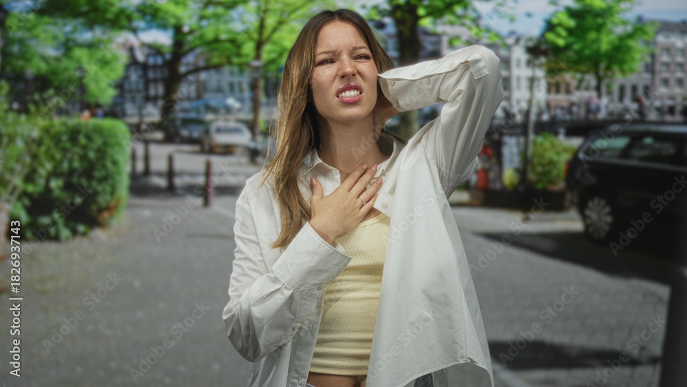 Fototapeta premium Woman clutching chest and hand on neck on city street, visible chest skin and pained face suggesting heartattack; distress health concern.