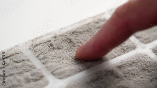 Dirty air conditioner filter panel and finger scraping off dust fibers on white table. Macro shot