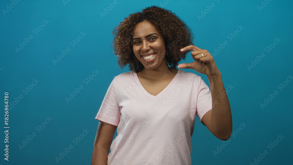 Fototapeta premium Young african american woman pinching a small gap between fingers in studio with turquoise backdrop; small size joy.