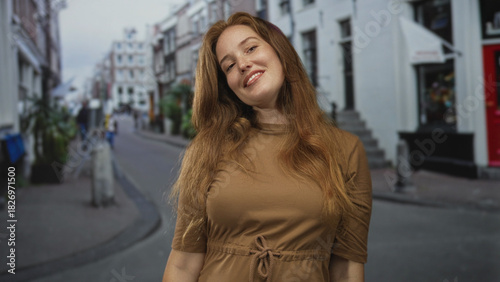 Smiling redheaded woman raises forearms on busy urban street lined with buildings; celebration joy.