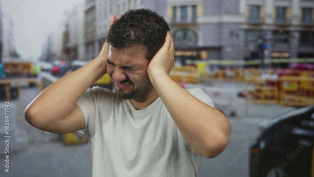 Fototapeta premium Young hispanic man wearing white tshirt pressing hands to ear on busy construction site street; stress.