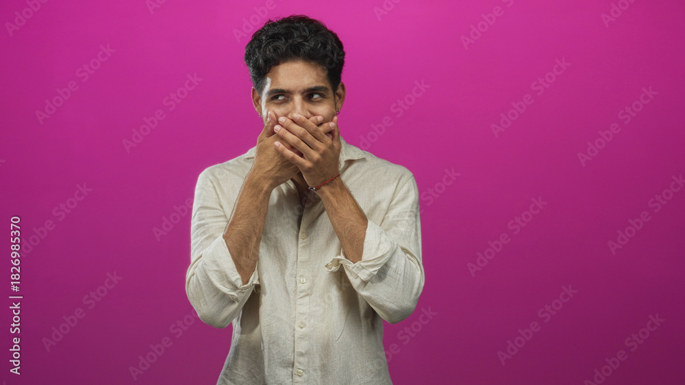 Obraz premium Young hispanic man hands covering mouth in studio with pink backdrop wearing beige linen shirt and small bracelet; playful surprise.