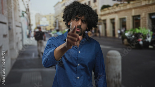 Картината върху платно Man points finger directly at camera on busy city street near bollard and parked motorcycles;accusation anger confrontation