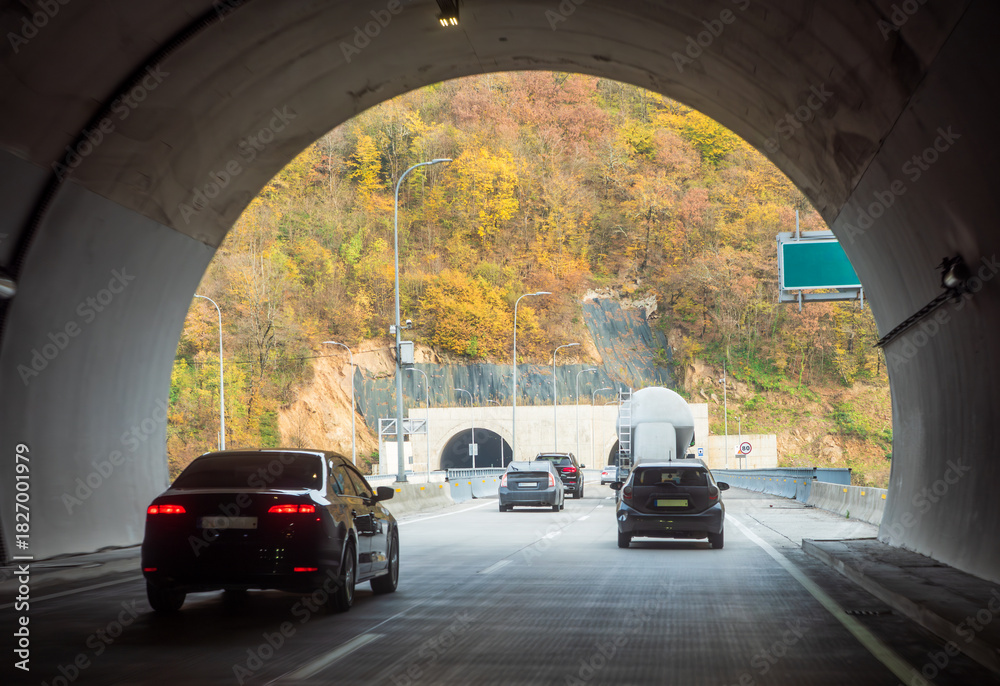 Fototapeta premium Cars driving through mountain tunnels in autumn, highway traffic in scenic landscape, road infrastructure in hilly terrain.