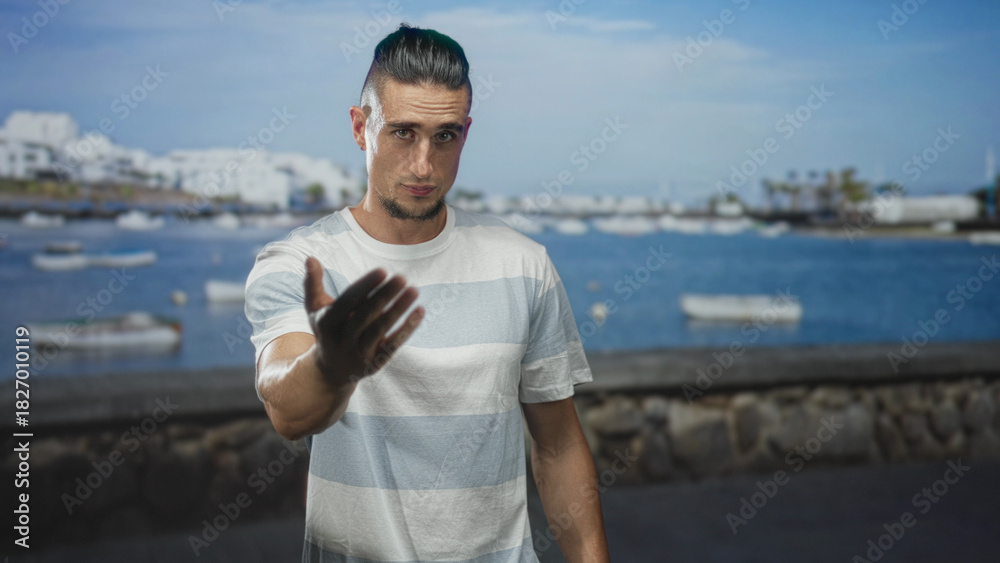 Fototapeta premium Man beckoning with outstretched hand on a seaside street by small boats and a stone harbor wall; inviting connection.
