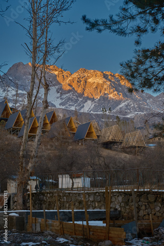 A-frame cabins on snowy hillside at sunrise, under construction, forest retreat with mountain view.
