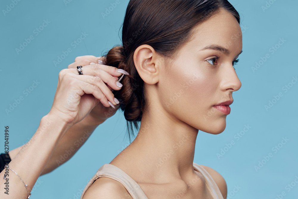 Fototapeta premium A young woman with a professional hairstyle being styled against a soft blue background, showcasing beauty and elegance in a modern setting