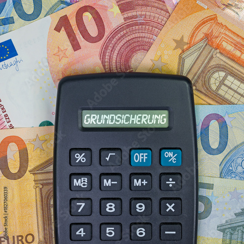 Taschenrechner mit dem Wort Grundsicherung im Display vor Geldscheinen