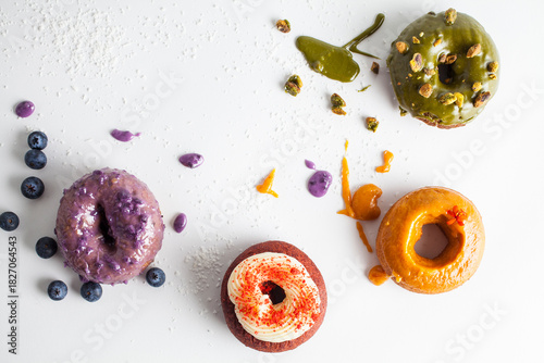 Colorful donuts with artistic glaze are abstractly splattered on a white table. 