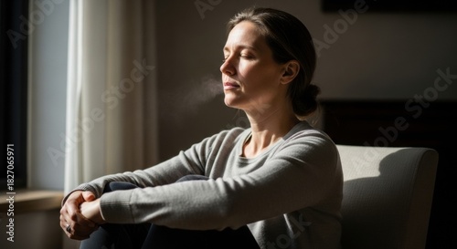 Calm woman with closed eyes exhaling visible breath while sitting in a sunlit room, practicing mindfulness and deep breathing for relaxation and mental wellbeing