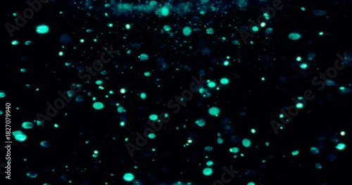 Particles float in water over a dark background, reflecting top light in green and blue hues, creating a glittering, halo-like, cosmic universe effect.