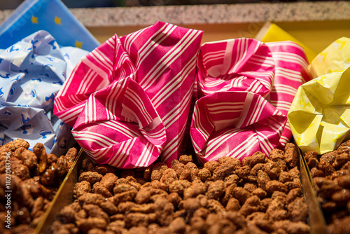 A tray filled with candied nuts at a christmas market stall, surrounded by colorful paper bags ready for serving.
