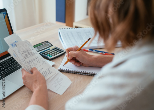 Woman checking paper bills while calculating expenses at home. Over-shoulder view of pencil and calculator. Home budget, smart money management and personal finance planning concept