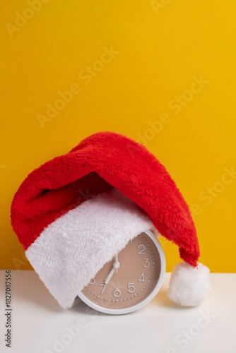 Alarm clock covered with santa hat on color background. Holiday Countdown