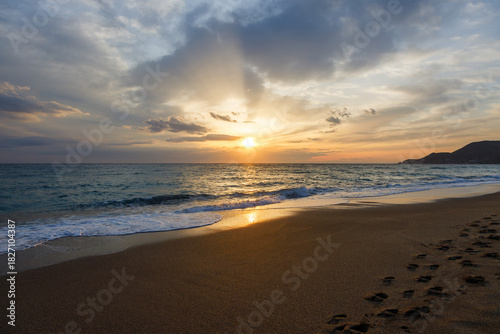 Fototapeta Naklejka Na Ścianę i Meble -  Warm golden rays of the setting sun reflect on the wet sand of Kleopatra Beach in Alanya, Turkey. Gentle waves touch the shore while the footprints in the sand fade away in the evening light