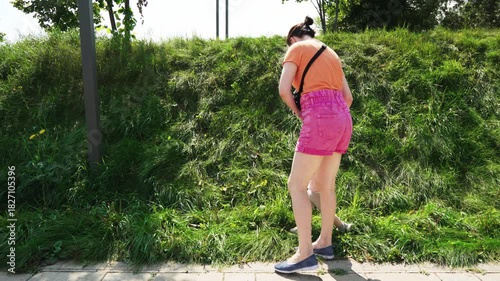 Woman holding child picking fruit on a sunny day in a park surrounded by greenery