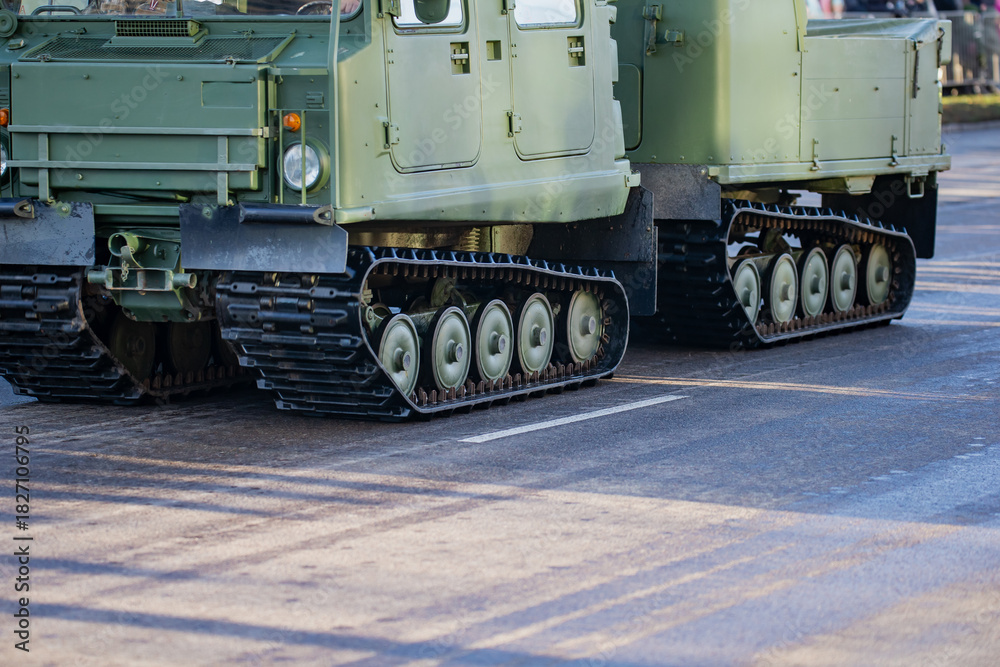 Obraz premium Tracked military transport vehicles with connected chassis and visible suspension components moving along an urban roadway during defense mobility readiness