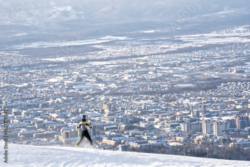 Skier on snowy mountain overlooking city in winter haze