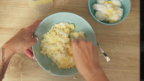 Hands are seen stirring a mixture in a blue bowl on a wooden table.