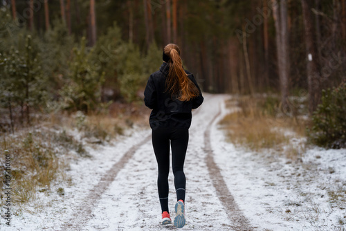 Fitness training in a winter landscape, female runner moving through icy scenery with focus on health and personal discipline.