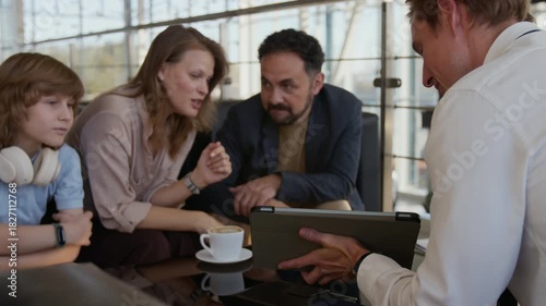 Over shoulder shot of car salesman pointing at tablet screen while talking to excited Caucasian family choosing new car in dealership