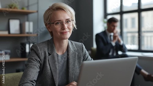 Confident Blonde Businesswoman in Glasses Smiling at Camera, Working on Laptop in Modern Office Environment