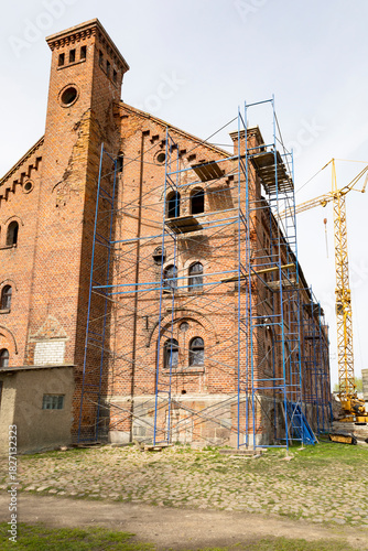 Restoration of historic brick church with scaffolding and crane present, An aged brick church undergoing refurbishment with construction equipment and urban surroundings