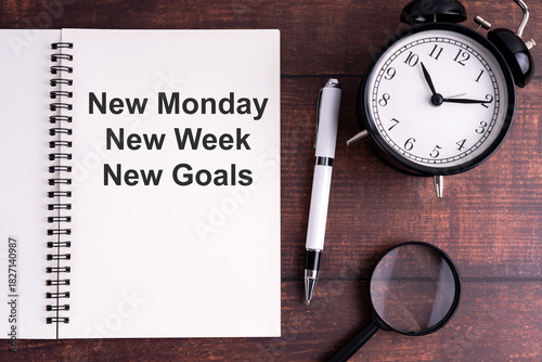 Minimal workspace with notebook, inspirational quote, classic alarm clock, pen, and magnifying glass on wooden desk for motivation and productivity themes.