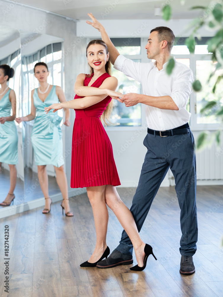 Naklejka premium Smiling elegant young adult couple, bride and groom rehearsing sensual wedding dance in studio under guidance of professional female choreographer in bright studio..