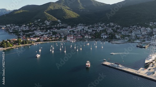 Coastal town of Tivat, Montenegro with sailboats anchored in a calm bay at the foot of green mountains – aerial 4K drone view of waterfront houses, marina entrance and scenic Adriatic landscape