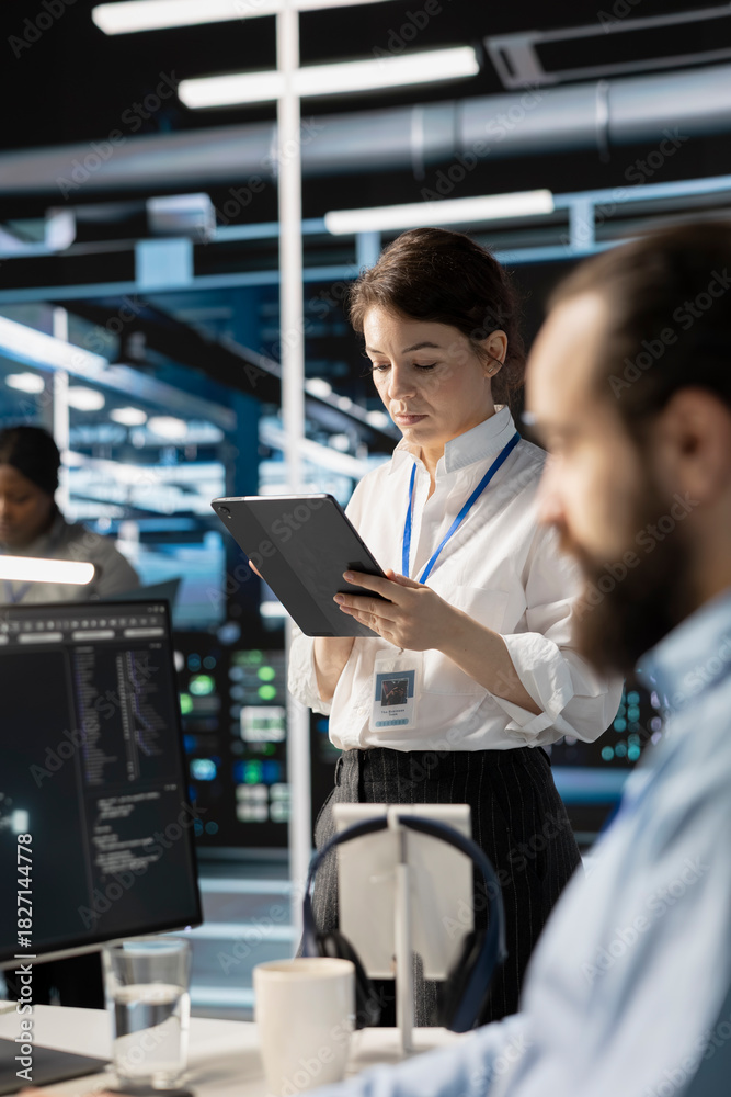 Naklejka premium Engineer using tablet in data center to deploy server virtualization updates, configuring equipment using software tools. IT worker reviewing hardware analytics, ensuring reliable network operations