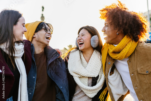 Diverse group of young friends having fun together outdoors on winter. Millennial student people laughing walking in city street enjoying day off. Youth community and friendship concept.