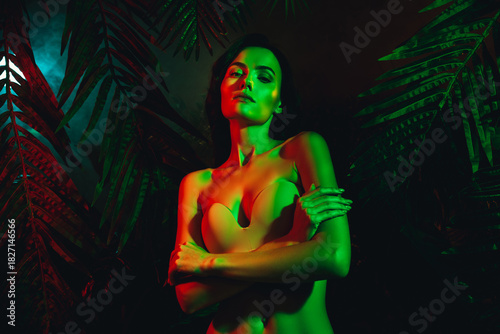Portrait of a sensual young woman illuminated by vibrant neon lights surrounded by tropical foliage