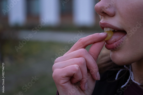 Close up of woman placing throat lozenge in mouth outdoors