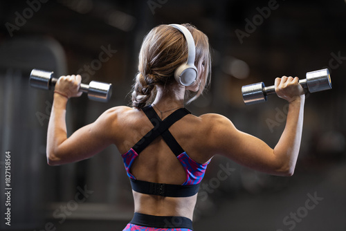 Girl performing dumbbell shoulder lifts in a gym during a workout session focusing on fitness and strength training